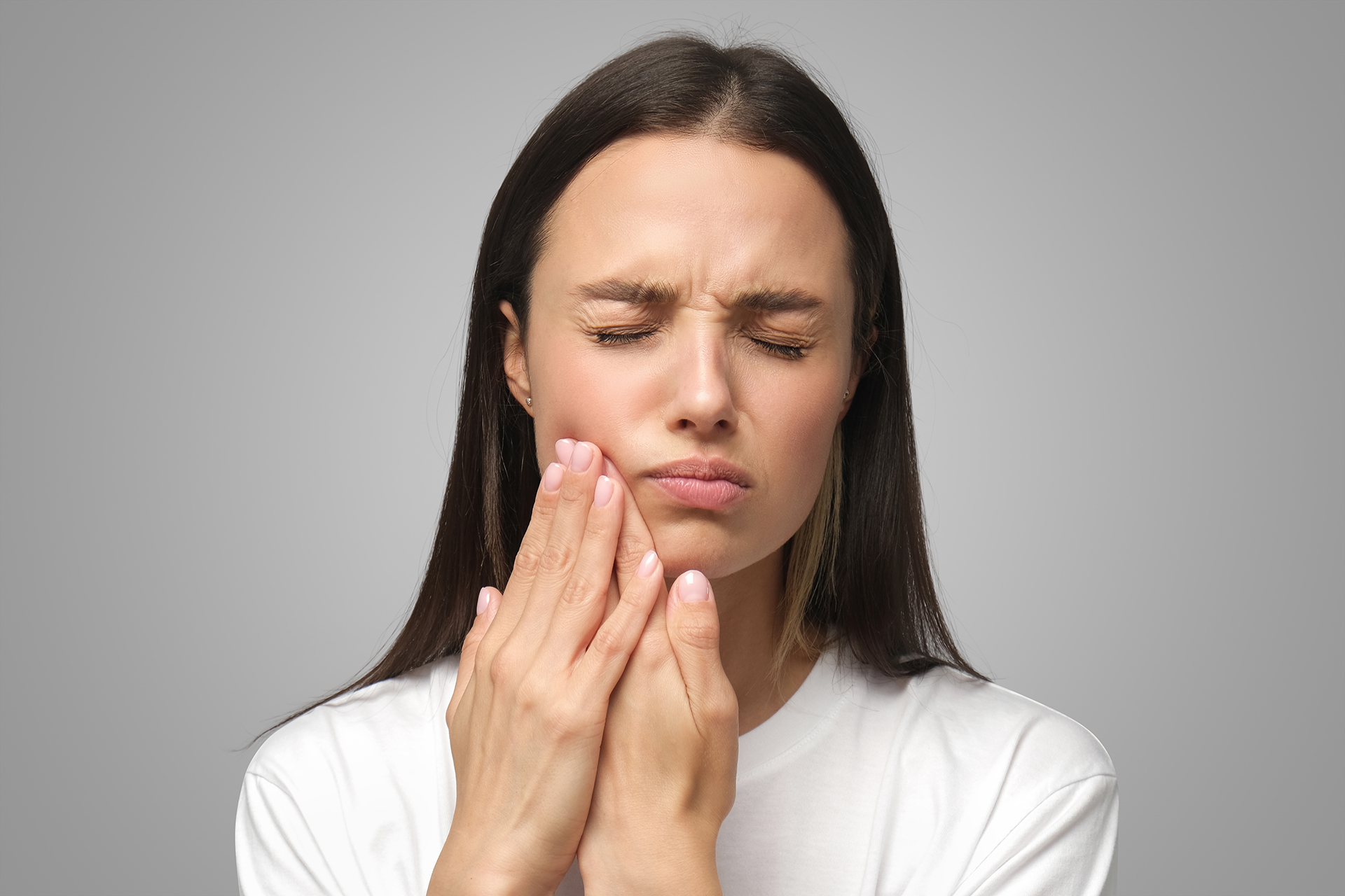 The image shows a young woman with her eyes closed and her hand on her face, appearing to be experiencing pain or discomfort, possibly related to dental care given the context of her facial expression and gesture.