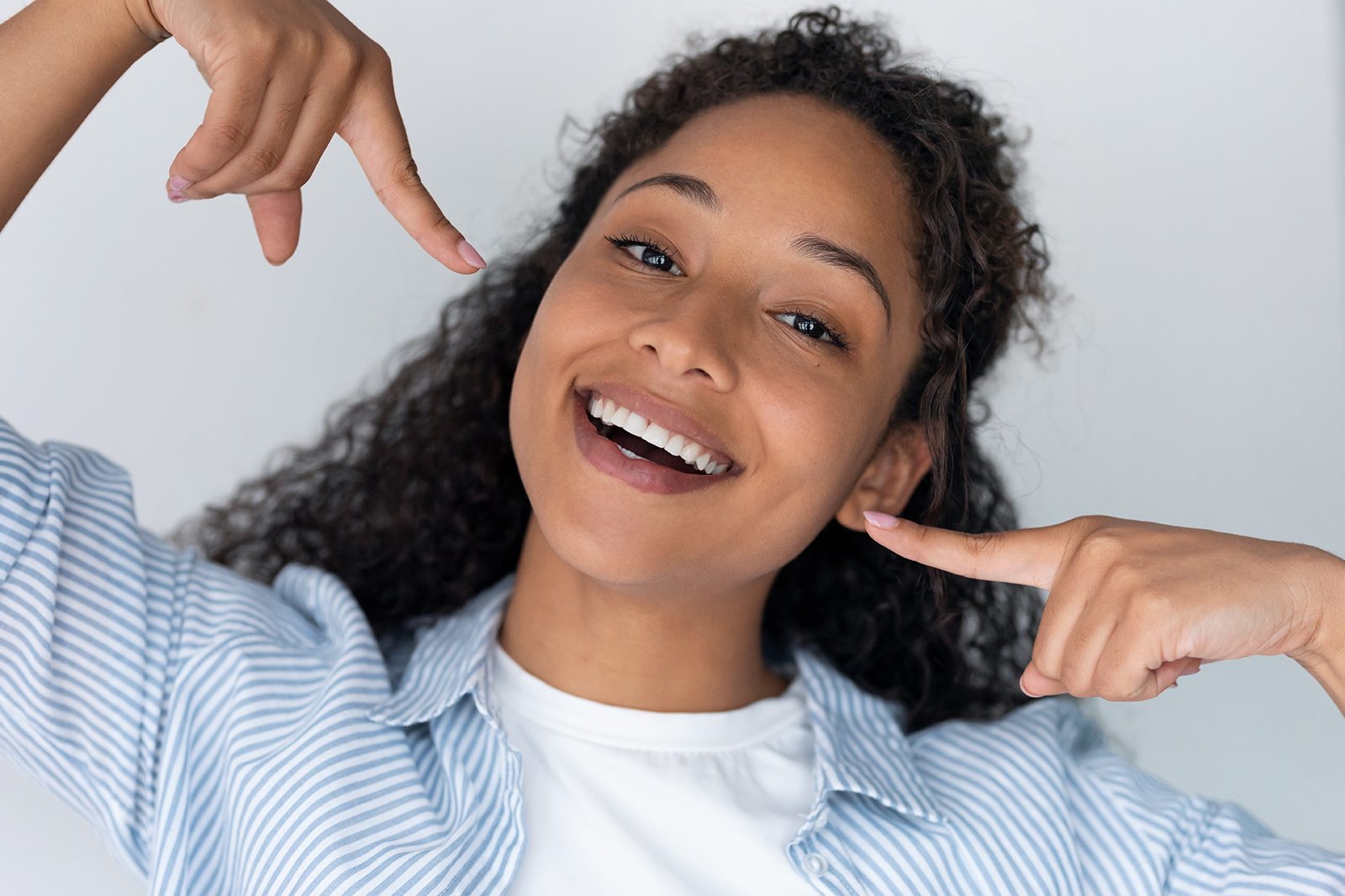 A young woman with a bright smile, making a peace sign gesture with her hand, against a white background.