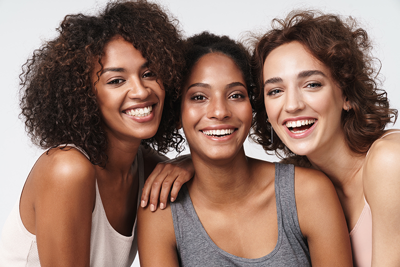 A group of four women with different hairstyles and facial expressions, smiling at the camera against a plain background.